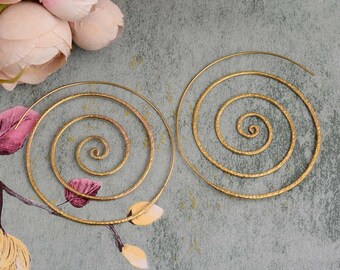 May include: A pair of gold-toned spiral hoop earrings. The earrings are made of a hammered metal and have a textured finish.