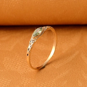 Può includere: Un anello d'oro con un design delicato e una pietra preziosa verde al centro.