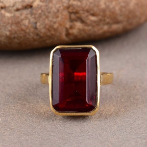 Peut inclure: Une bague en or avec une grande pierre rectangulaire rouge foncé.