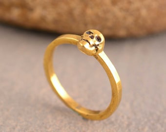 May include: A gold-toned ring with a small skull design. The ring is simple and minimalist.