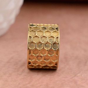 May include: A gold-coloured ring with a honeycomb pattern. The ring is made of metal and has a smooth, polished finish.
