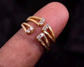 May include: Four gold-colored rings, each with a unique design featuring small, clear gemstones. The rings are displayed on a finger against a dark background, showcasing their intricate details and sparkling accents.