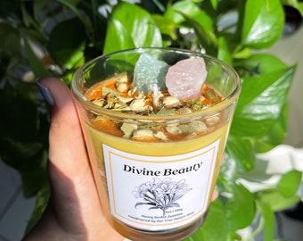 May include: A yellow candle with a label that reads "Divine Beauty" and "Honey Suckle Jasmine". The candle is topped with dried herbs and crystals.