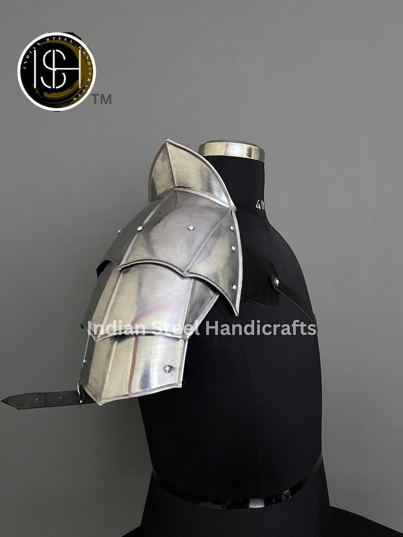 May include: Silver plated metal shoulder armour with a layered design. The armour is displayed on a black mannequin. The text "Indian Steel Handicrafts" is visible on the mannequin.