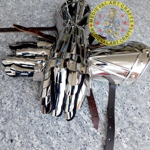May include: A pair of silver plated medieval gauntlets with a scale mail design. The gauntlets are attached to leather straps.