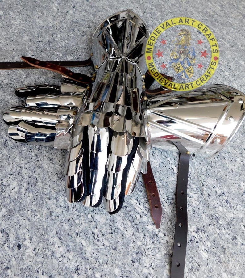May include: A pair of silver plated medieval gauntlets with a scale mail design. The gauntlets are attached to leather straps.