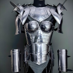 Peut inclure: Une armure en m&eacute;tal argent&eacute; avec une jupe en cotte de mailles et des prot&egrave;ge-bras assortis. L'armure est expos&eacute;e sur un mannequin.