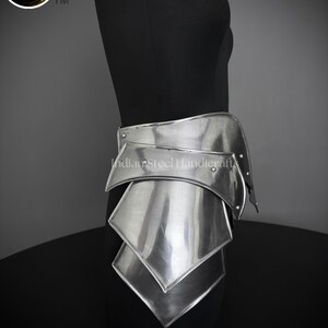 May include: Silver metal armor for the waist and hips, with a series of overlapping plates. The armor is displayed on a black mannequin.