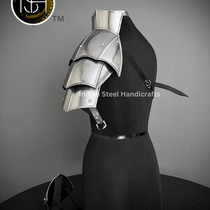K&ouml;nnte beinhalten: Silberbeschichteter Schulterpanzer aus Metall mit einem mehrschichtigen Design. Die R&uuml;stung ist an einem schwarzen Mannequin mit einem schwarzen Lederriemen befestigt. Der Text "Indian Steel Handicrafts" ist auf dem Mannequin sichtbar.