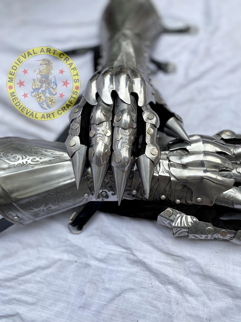Puede incluir: Primer plano de un guante medieval de acero pulido. El guante presenta placas articuladas, afiladas puntas en los dedos y dise&ntilde;os grabados. Se puede ver el texto "MEDIEVAL ART CRAFTS". Una pieza de armadura hist&oacute;rica.