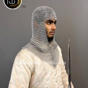 May include: A person wearing a white coif made of chainmail, a white padded jacket, and holding a long, thin, silver-colored blade.