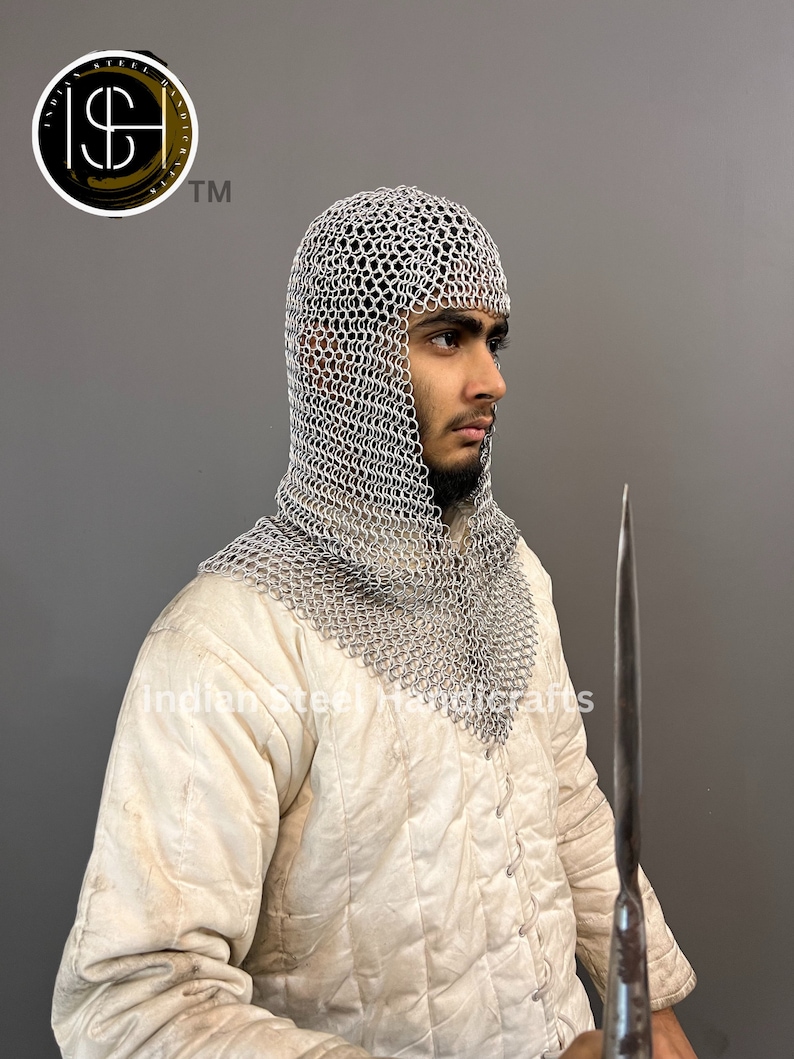 May include: A person wearing a white coif made of chainmail, a white padded jacket, and holding a long, thin, silver-colored blade.