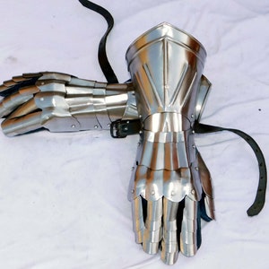 Puede incluir: Un par de guanteletes de metal plateado con dedos articulados y una correa de cuero. Los guanteletes están diseñados para proteger las manos y las muñecas durante el combate.