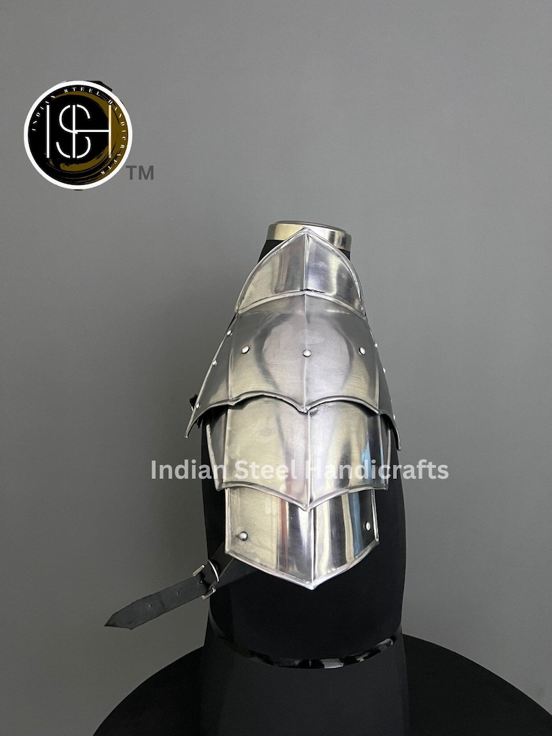 May include: Silver plated steel shoulder armour with a decorative design. The armour is attached to a black leather strap. The armour is on a black mannequin. The text "Indian Steel Handicrafts" is visible in the image.