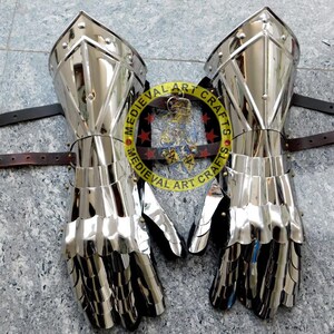 May include: A pair of silver plated medieval gauntlets with leather straps. The gauntlets are made of metal plates and have a pointed design. The gauntlets are for the left and right hand.