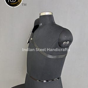 May include: A black leather shoulder armour with metal plates and straps. The armour is displayed on a black mannequin. The text "Indian Steel Handicrafts" is visible on the image.