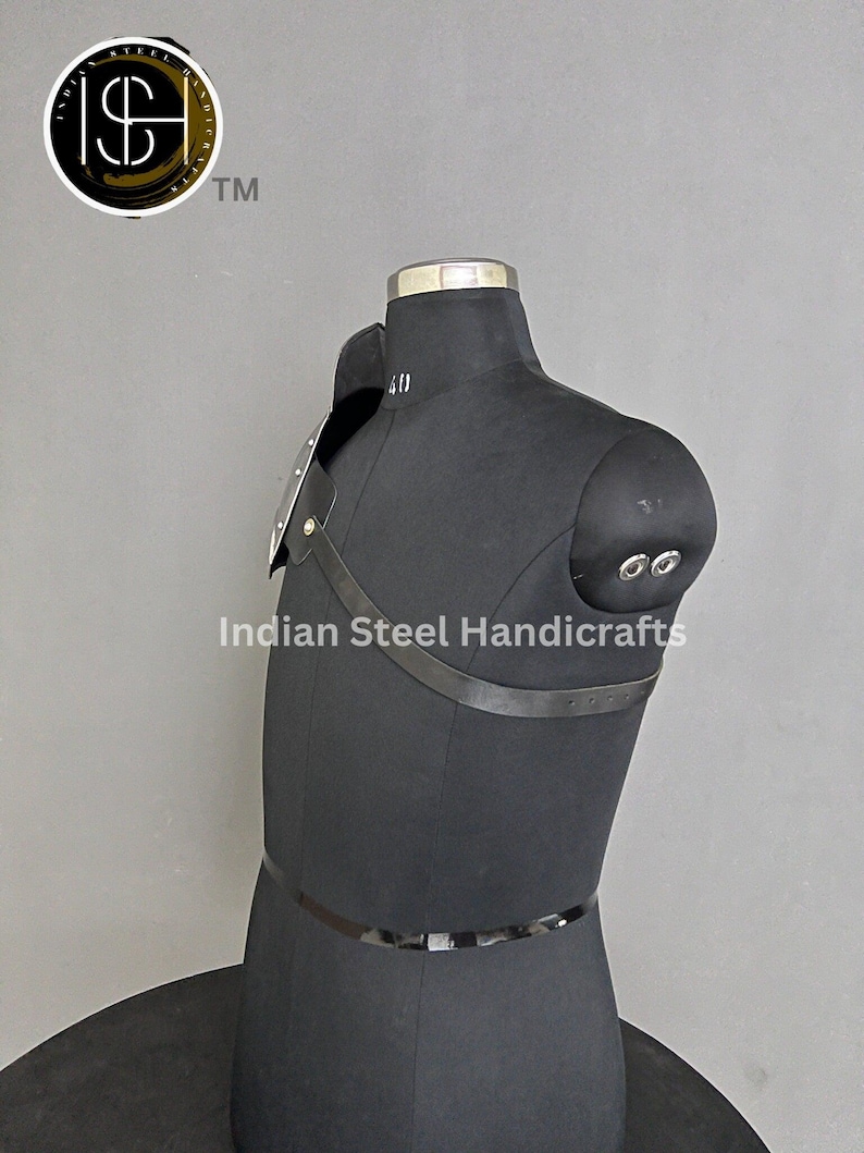 May include: A black leather shoulder armour with metal plates and straps. The armour is displayed on a black mannequin. The text "Indian Steel Handicrafts" is visible on the image.