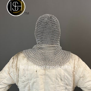 May include: A silver chainmail coif with a hood, worn over a white padded jacket. The coif is made of interlocking metal rings and covers the head and neck. The jacket has a quilted design and is worn for protection.