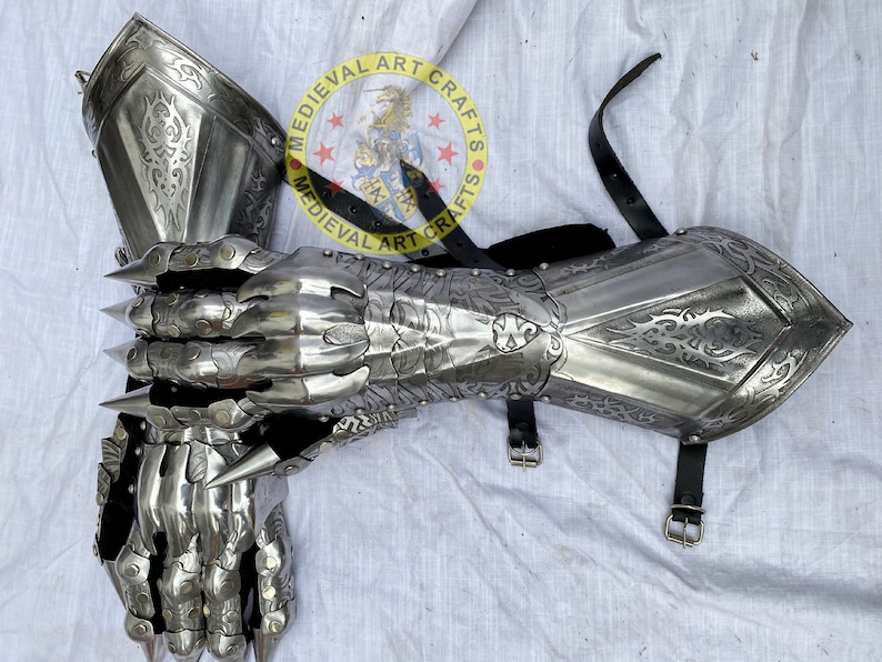 Puede incluir: Un par de guanteletes plateados con intrincados dise&ntilde;os grabados y afiladas p&uacute;as. Los guanteletes son de metal y cuentan con correas de cuero con hebillas. El logotipo de Medieval Art Crafts es visible.