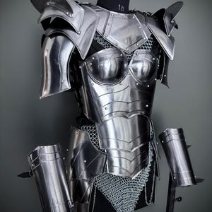 Peut inclure: Une armure en m&eacute;tal argent&eacute; avec une jupe en cotte de mailles et des prot&egrave;ge-bras assortis. L'armure est expos&eacute;e sur un mannequin.