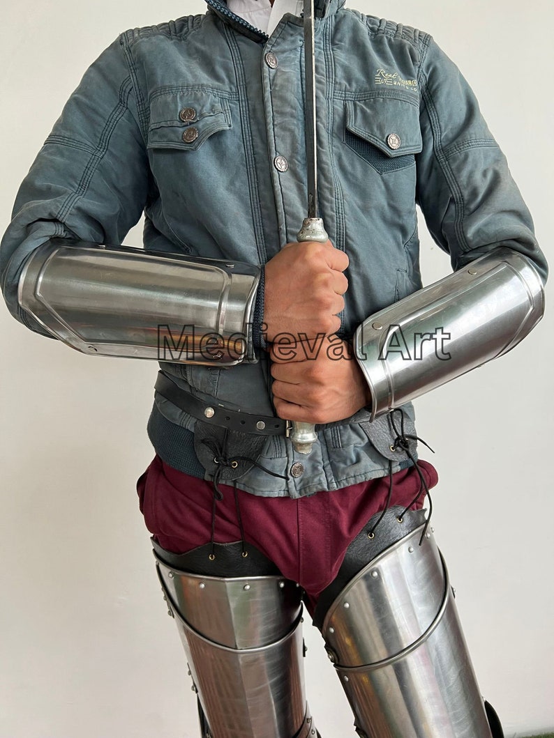May include: A pair of silver metal arm guards and a pair of silver metal leg guards. The arm guards are worn on the forearms and the leg guards are worn on the thighs. The guards are made of metal plates that are connected by leather straps.