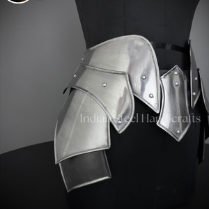 May include: Silver metal hip armor with a layered design. The armor is made of multiple plates that are connected together with rivets. The armor is worn on a black mannequin.