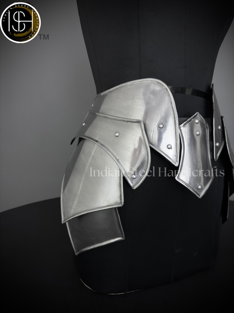 May include: Silver metal hip armor with a layered design. The armor is made of multiple plates that are connected together with rivets. The armor is worn on a black mannequin.