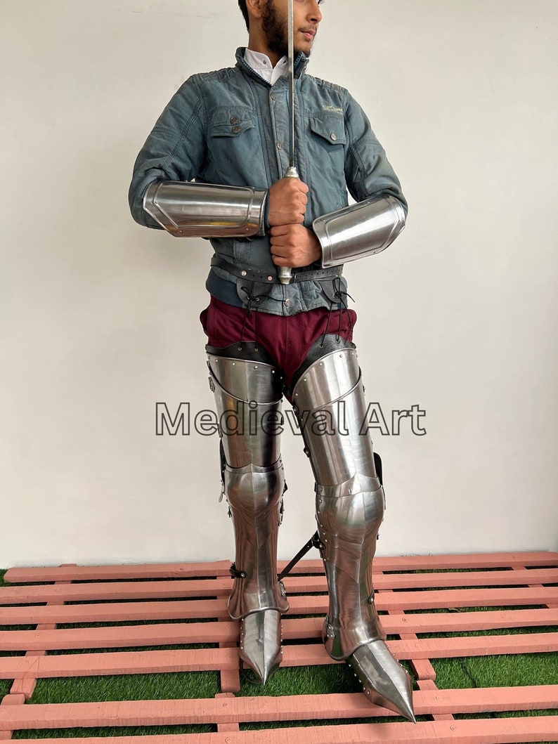 May include: A person wearing silver medieval armor, including leg armor with pointed toes, and matching arm armor. The person is holding a sword and the text "Medieval Art" is visible in the image.