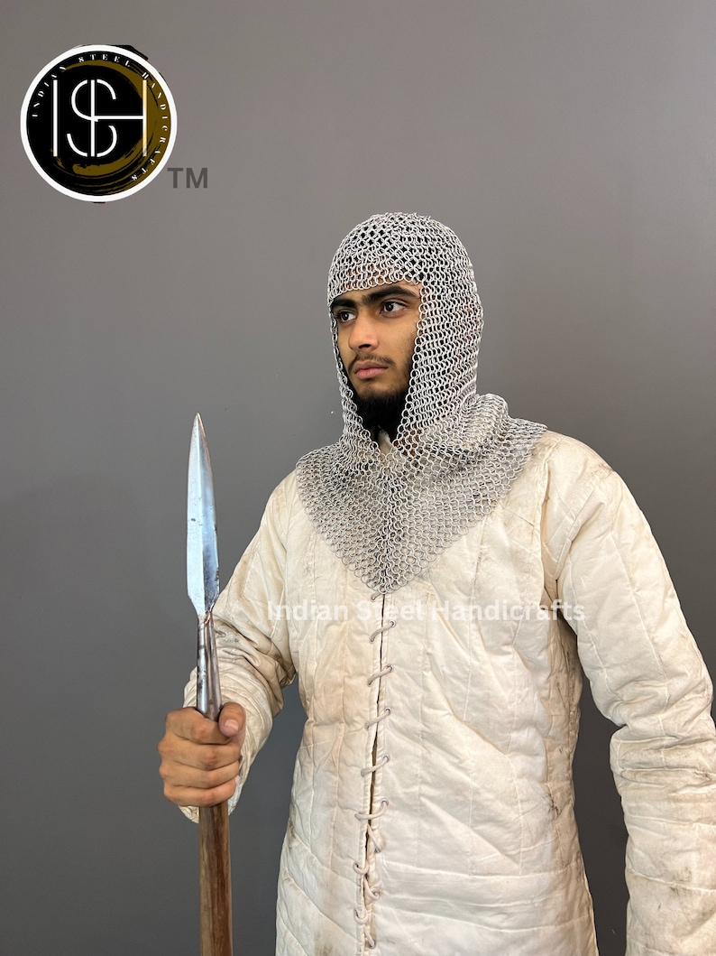 May include: A person wearing a white padded jacket and a silver chainmail coif, holding a long, silver-tipped spear. The text "Indian Steel Handicrafts" is visible on the jacket.