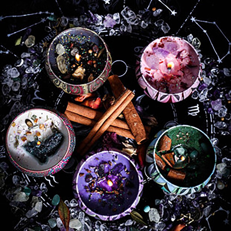 May include: Five candles with different colored waxes and embedded crystals, surrounded by cinnamon sticks and small stones on a black background with zodiac symbols.