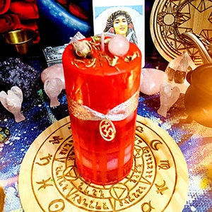 May include: A red candle with a white ribbon and a small gold charm. The candle is surrounded by pink and clear crystals and a wooden circle with a design on it.