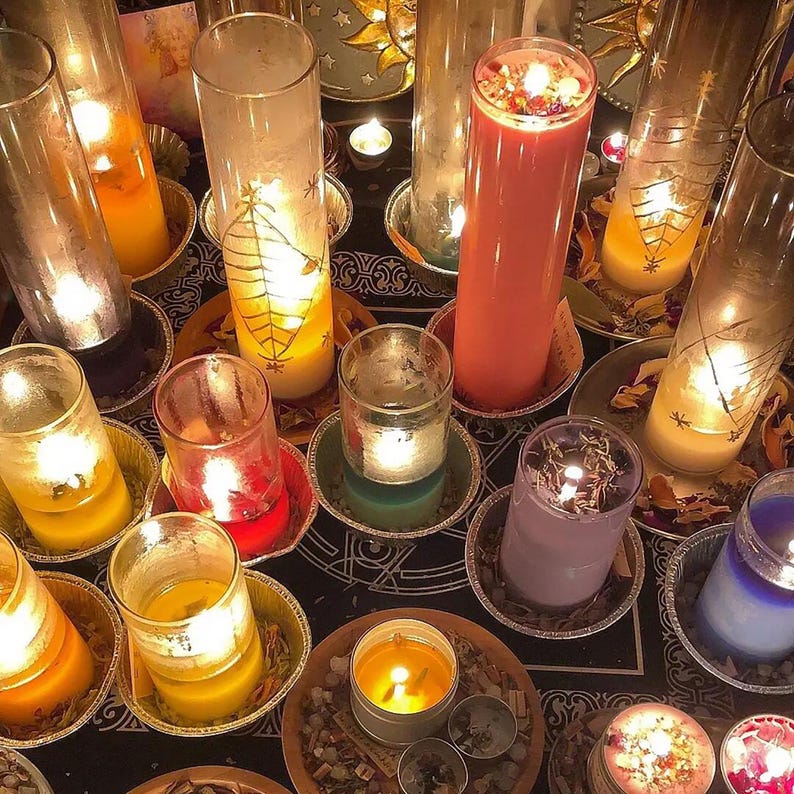 Pu&ograve; includere: Una collezione di candele di vari colori e dimensioni, tra cui rosso, giallo, viola e blu, sono disposte su una superficie nera con accenti decorativi. Le candele sono accese e proiettano un bagliore caldo.