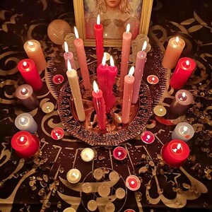 Pu&ograve; includere: Primo piano di un tavolo con una variet&agrave; di candele disposte in cerchio. Le candele sono di diversi colori, tra cui rosso, rosa, bianco e viola. Ci sono anche diversi piccoli oggetti rotondi sparsi intorno alle candele.