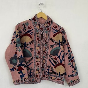 May include: A pink embroidered jacket with a floral pattern in shades of blue, green, and red. The jacket has a mandarin collar and a button closure.