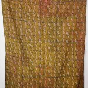 Könnte beinhalten: Großes, rechteckiges Textil mit einem sich wiederholenden Paisley-Muster in Olivgrün, Beige und Schwarz. Der Stoff hat ein Patchwork-Design mit sichtbaren Nähten. Die obere rechte Ecke hat einen rot-rosa Abschnitt.