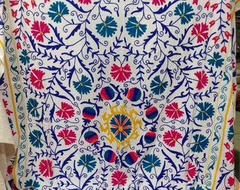 May include: White cotton fabric with a colorful floral embroidery design. The embroidery features blue, pink, yellow, and green flowers and vines.