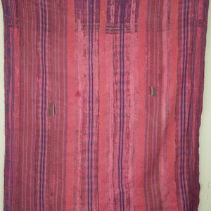 May include: A pink and purple striped textile, possibly a blanket or throw, with a vertical pattern. The fabric shows signs of wear, with visible stitching and colour variations. The textile is rectangular in shape and appears to be handmade.