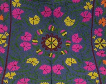 May include: A blue fabric square with a floral design. The flowers are pink, yellow, and orange. The center of the square has a circular design with a maroon center and yellow petals.