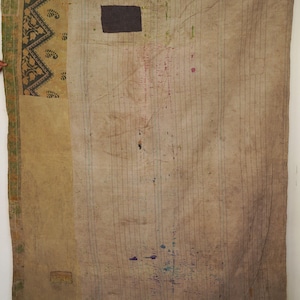 May include: A vintage, rectangular textile with a patchwork design. The quilt features a beige background with vertical lines and a dark brown square patch. The edges have decorative patterns in green, black, and gold.