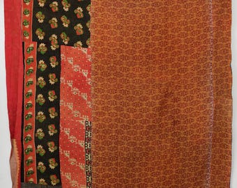 May include: A rectangular textile featuring a patchwork design with a large section of orange fabric with a repeating pattern, alongside panels of black fabric with green and red paisley motifs, and a red fabric strip with a green geometric border.