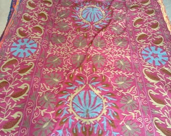 May include: A pink fabric throw blanket with intricate embroidery in brown, blue, and yellow. The design features floral patterns and paisley motifs.