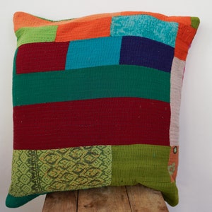 Könnte beinhalten: Ein farbenfrohes Patchwork-Kissen mit verschiedenen Farben wie Grün, Rot, Orange, Blau und Pink. Das Kissen besteht aus Stoffresten, die in rechteckiger Form zusammengenäht wurden.