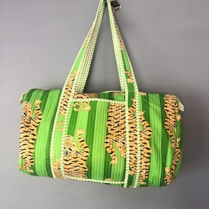 以下が含まれることがあります： 緑とオレンジのストライプのダッフルバッグに虎のプリントが施されています。バッグにはハンドルが2つ付いています。