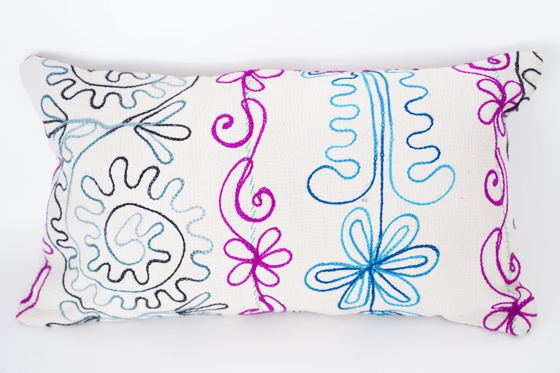 May include: White pillow with embroidered floral and paisley designs in blue, pink, and black thread.