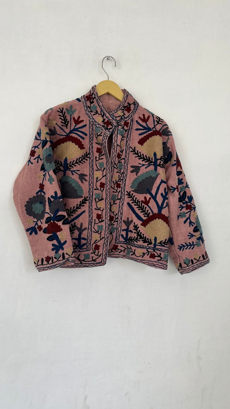 May include: A pink embroidered jacket with a floral pattern in shades of blue, green, and red. The jacket has a mandarin collar and a button closure.