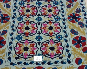 May include: A white cotton rug with a blue, red, pink, and gold floral pattern. The rug has a border with a repeating design of leaves and flowers. The number "39" is written in the lower center of the rug.