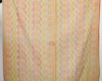 Op de afbeelding: Een vintage quilt met een herhalend patroon van gele en witte bloemen en geometrische ontwerpen op een roze achtergrond. De quilt heeft een rand van gele en oranje bloempatronen. De quilt is rechthoekig en lijkt van stof te zijn.