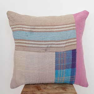 Puede incluir: Una almohada de patchwork con un borde rosa, que presenta un patrón de cuadros azul y blanco, rayas azules y blancas y un fondo beige.