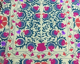 May include: A cream-colored fabric with intricate embroidery featuring a central tree design with blue, pink, and red flowers and leaves. The border is decorated with a repeating pattern of blue, pink, and red flowers.