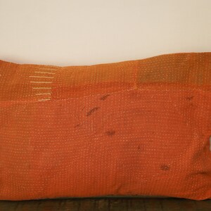 May include: A large, orange, rectangular pillow with a patchwork design. The pillow is made of a soft, quilted fabric and has a subtle sheen.